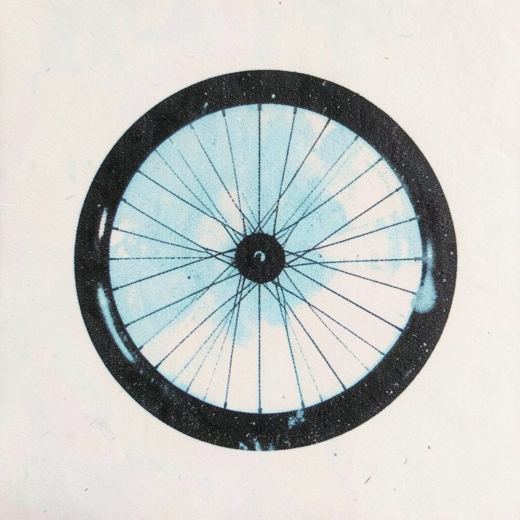 Two-ink risograph print of a bicycle wheel in black and pale blue against a soft off-white background, printed texture visible, no text or logos